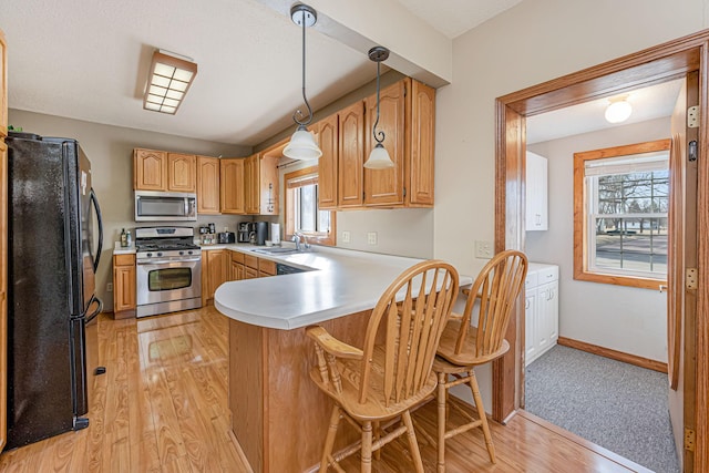 kitchen with a peninsula, a sink, light countertops, appliances with stainless steel finishes, and light wood-type flooring