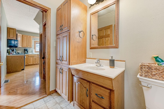 bathroom featuring visible vents, toilet, vanity, a textured wall, and a textured ceiling