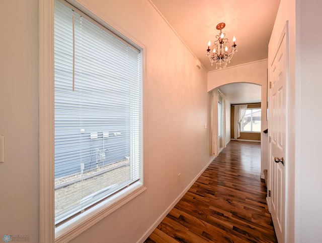 hallway with dark wood-style floors, baseboards, an inviting chandelier, arched walkways, and crown molding