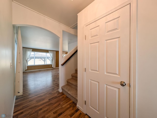 staircase with wood finished floors, arched walkways, and baseboards