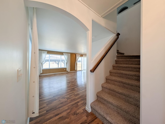 staircase with arched walkways, baseboards, and wood finished floors