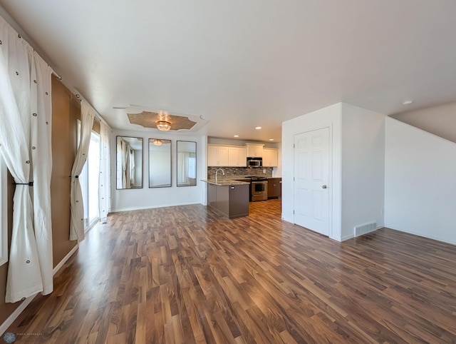 unfurnished living room with visible vents, baseboards, recessed lighting, dark wood-style floors, and a sink