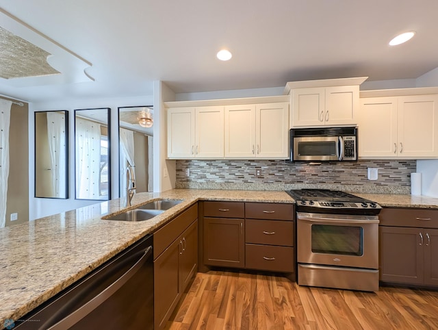 kitchen with light stone countertops, stainless steel appliances, light wood-type flooring, and a sink