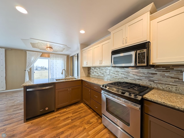 kitchen featuring a sink, stainless steel appliances, a peninsula, decorative backsplash, and light stone countertops