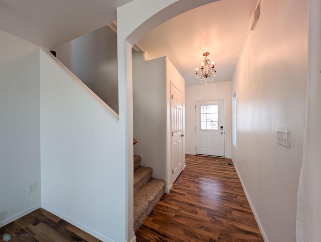 doorway to outside with arched walkways, a notable chandelier, wood finished floors, and stairs