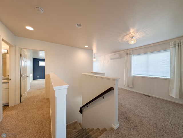 hallway featuring a wall mounted AC, an upstairs landing, visible vents, and light carpet