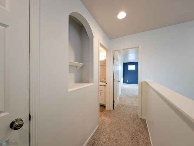 hallway featuring light colored carpet and baseboards