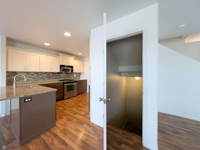 kitchen featuring light stone counters, decorative backsplash, appliances with stainless steel finishes, dark wood-style floors, and a sink