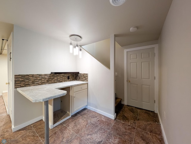 interior space featuring tasteful backsplash, stone finish flooring, baseboards, light countertops, and white cabinetry