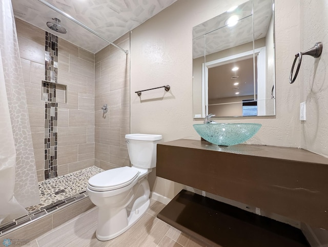 bathroom featuring vanity, a tile shower, tile patterned floors, toilet, and a textured wall