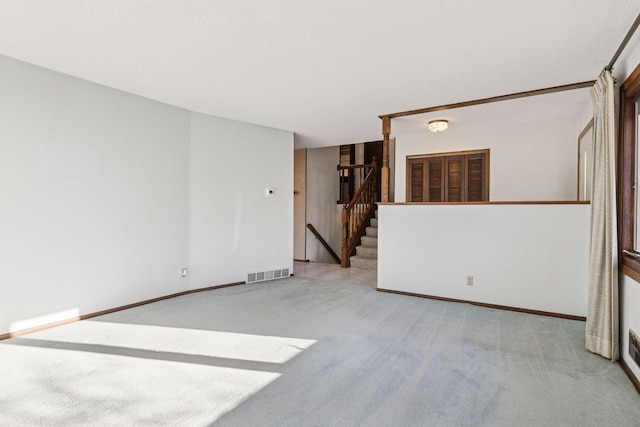 empty room featuring visible vents, baseboards, light colored carpet, and stairs