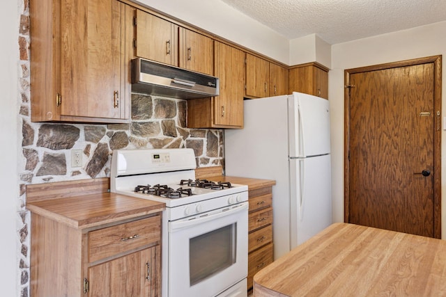 kitchen with under cabinet range hood, white appliances, a textured ceiling, and brown cabinetry