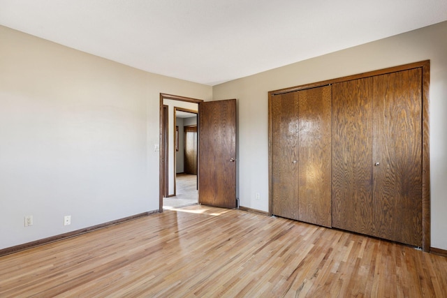 unfurnished bedroom featuring light wood-style floors, a closet, and baseboards