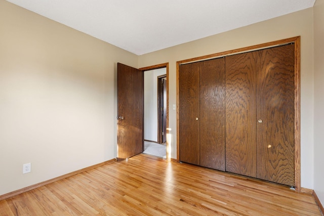 unfurnished bedroom featuring a closet, light wood-type flooring, and baseboards