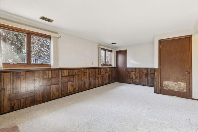 carpeted spare room featuring visible vents, wooden walls, and wainscoting