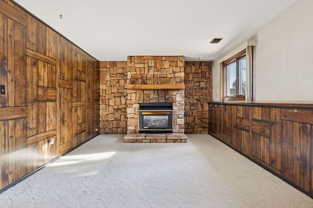 unfurnished living room featuring a stone fireplace, wooden walls, visible vents, and carpet floors