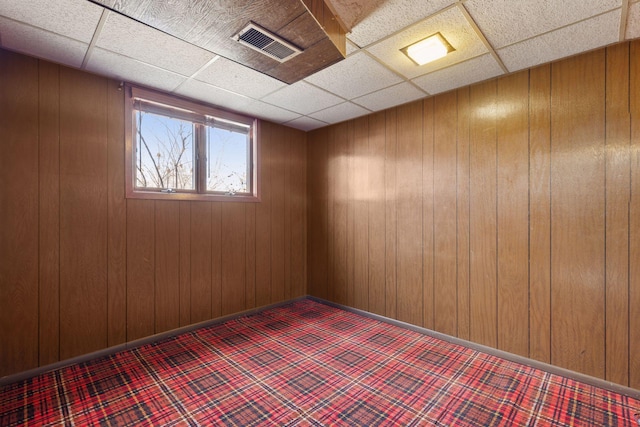 spare room featuring a drop ceiling, visible vents, baseboards, and wood walls