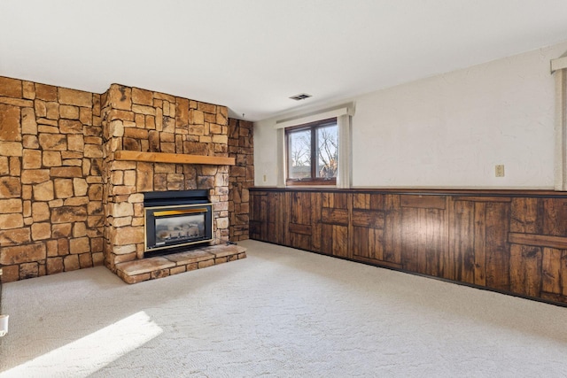 unfurnished living room with a wainscoted wall, carpet floors, a stone fireplace, and visible vents