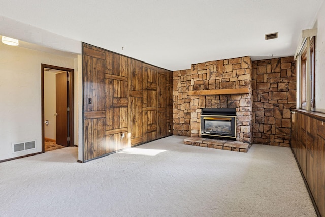 unfurnished living room with visible vents, wood walls, a stone fireplace, and carpet flooring