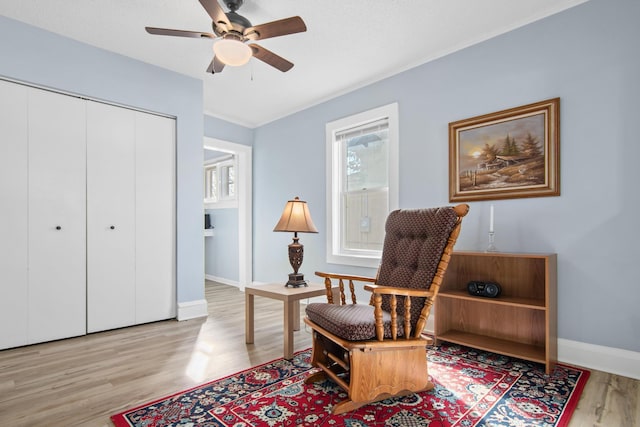 living area with crown molding, light wood-style floors, baseboards, and ceiling fan