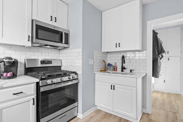 kitchen featuring a sink, light stone counters, appliances with stainless steel finishes, white cabinets, and light wood finished floors