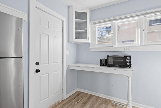 kitchen with visible vents, light wood finished floors, freestanding refrigerator, white cabinets, and glass insert cabinets