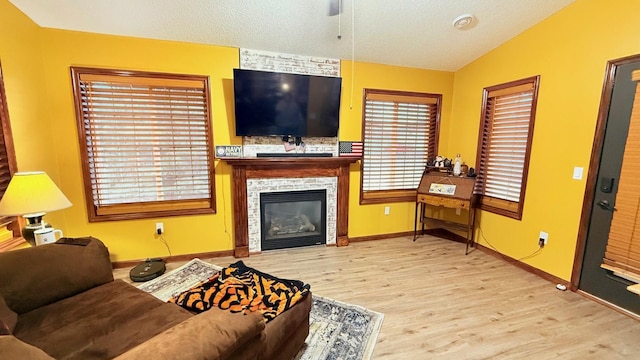 living area featuring a glass covered fireplace, lofted ceiling, wood finished floors, and a textured ceiling