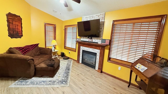 living room with a textured ceiling, a large fireplace, light wood finished floors, lofted ceiling, and ceiling fan