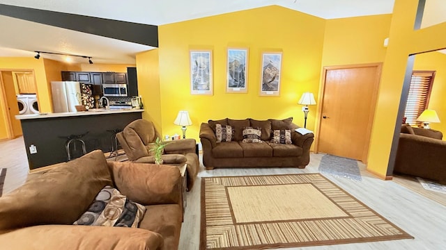 living room with lofted ceiling, washing machine and dryer, light wood finished floors, and track lighting