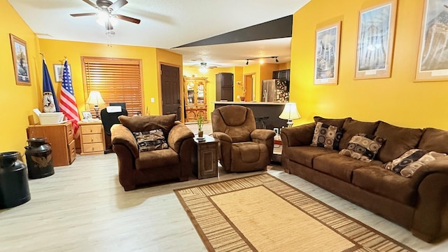 living room with light wood-type flooring, a ceiling fan, and vaulted ceiling