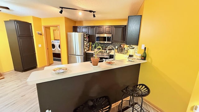 kitchen featuring light wood-style flooring, stainless steel appliances, a peninsula, light countertops, and washing machine and clothes dryer