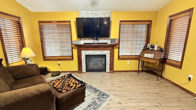 living room featuring a glass covered fireplace, wood finished floors, baseboards, and a textured ceiling