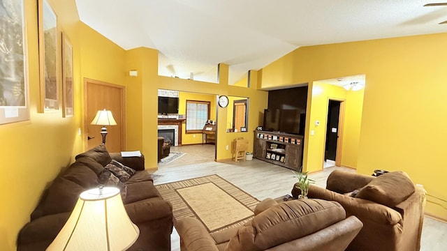 living room with a fireplace with flush hearth, ceiling fan, light wood-style floors, and vaulted ceiling