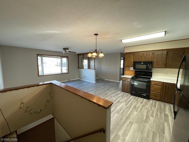 kitchen featuring visible vents, brown cabinets, black appliances, light wood finished floors, and light countertops