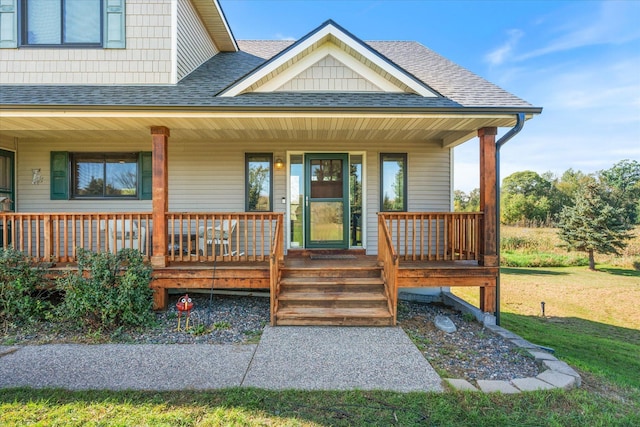 view of exterior entry featuring a yard, covered porch, and roof with shingles