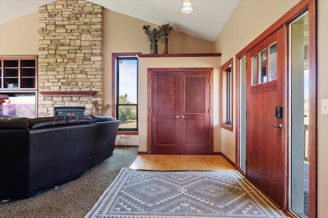 foyer entrance with a stone fireplace, vaulted ceiling, baseboards, and light wood-type flooring