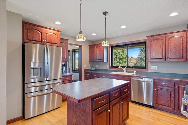 kitchen featuring a sink, dark countertops, appliances with stainless steel finishes, light wood finished floors, and hanging light fixtures