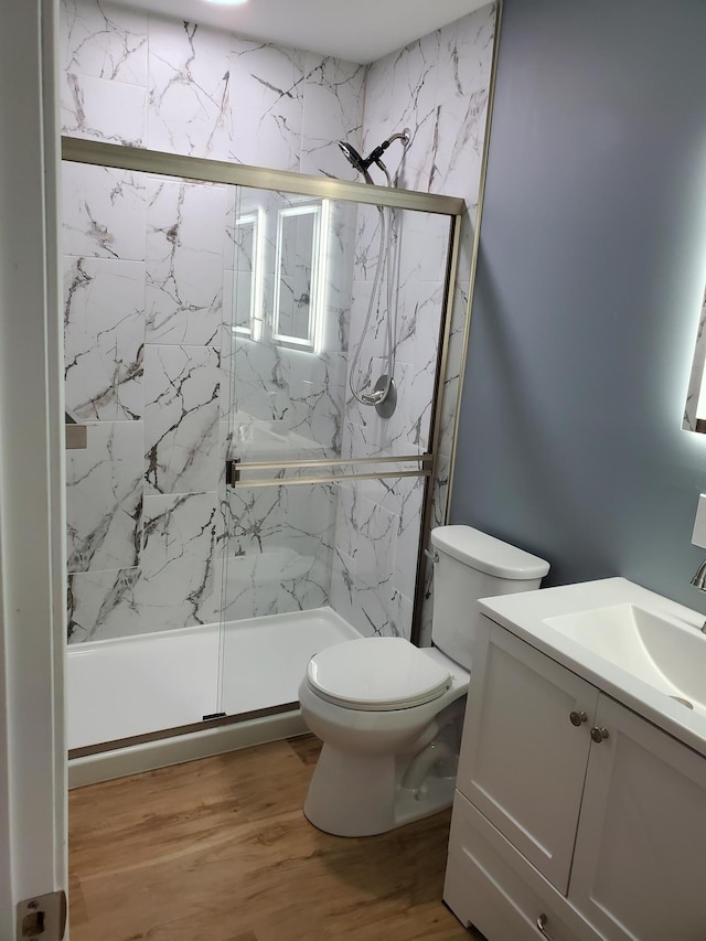 bathroom with a marble finish shower, toilet, vanity, and wood finished floors