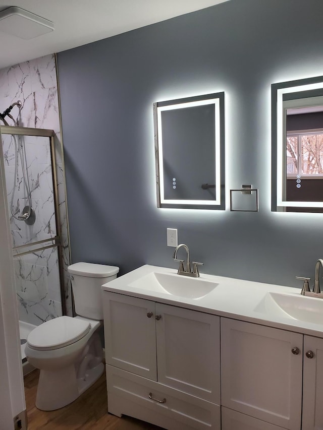 bathroom with a marble finish shower, double vanity, toilet, and a sink