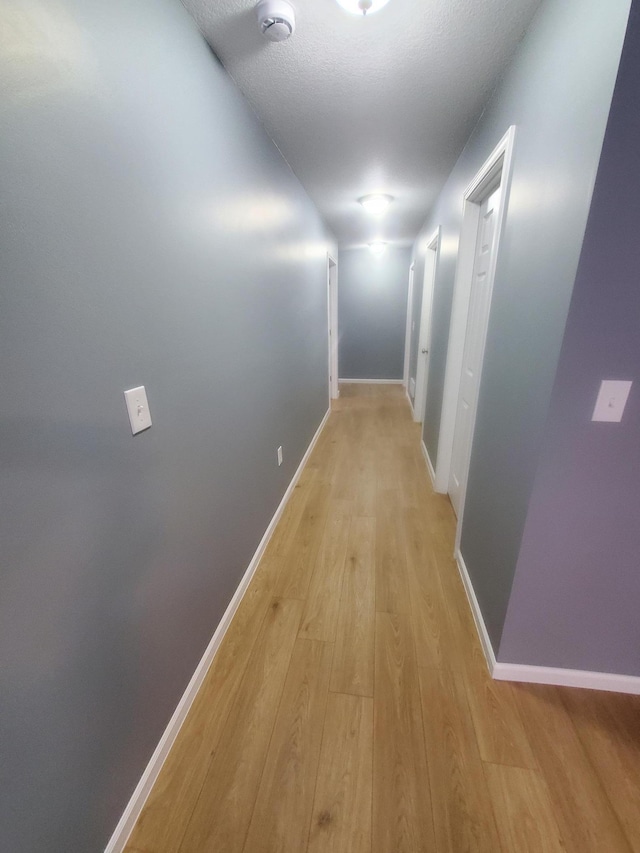 corridor featuring light wood-style floors, baseboards, and a textured ceiling