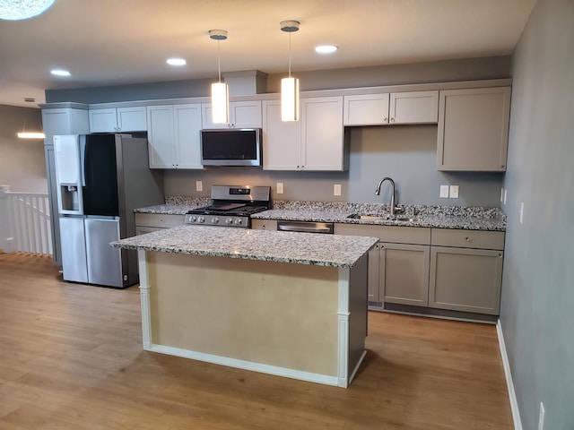 kitchen featuring a kitchen island, light wood-style flooring, appliances with stainless steel finishes, hanging light fixtures, and a sink