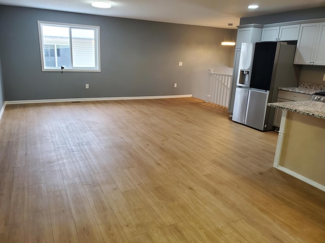 kitchen featuring light stone counters, light wood-style floors, stainless steel refrigerator with ice dispenser, and baseboards