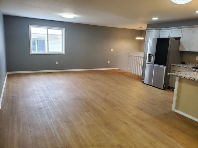 kitchen with baseboards, light stone countertops, light wood-style floors, and stainless steel fridge with ice dispenser