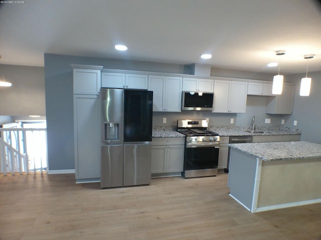 kitchen with baseboards, light stone counters, light wood-style flooring, stainless steel appliances, and a sink