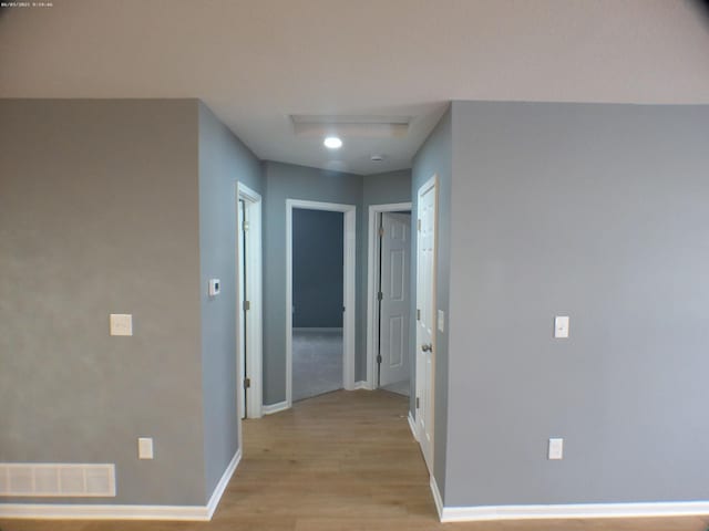 hall with attic access, baseboards, visible vents, and light wood finished floors