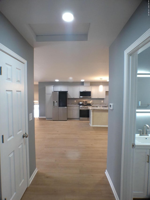 corridor with a sink, light wood-type flooring, baseboards, and recessed lighting