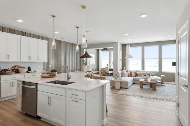 kitchen featuring light countertops, an island with sink, stainless steel dishwasher, white cabinets, and a sink