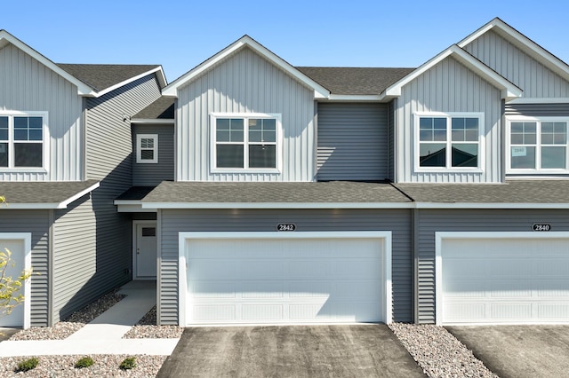 view of property with aphalt driveway, board and batten siding, roof with shingles, and an attached garage