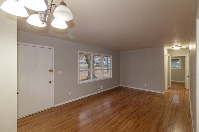 unfurnished living room featuring a notable chandelier, wood finished floors, visible vents, and baseboards