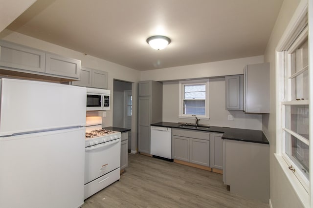 kitchen featuring dark countertops, gray cabinets, white appliances, and a sink